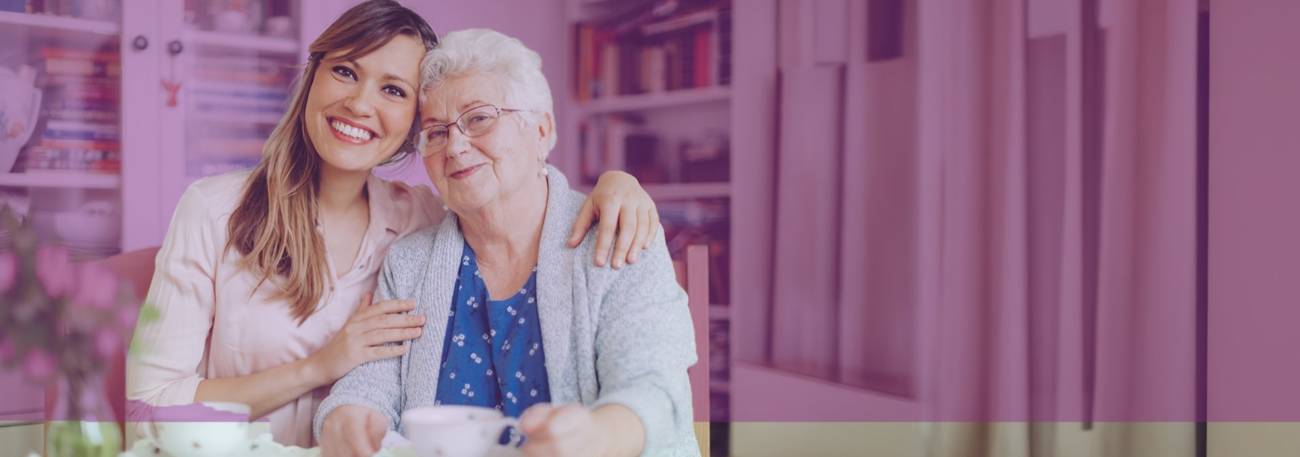 A young woman smiling with her arms around an elderly woman in her home with a purple tint on the background